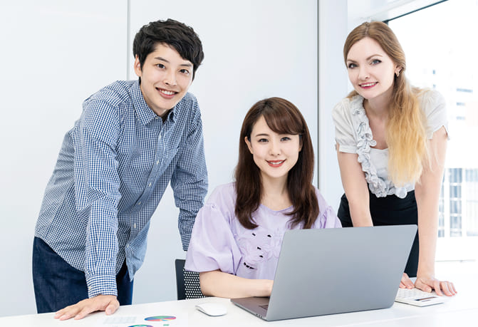 パソコンに向かい、外国人と一緒に学習する笑顔の学生の画像